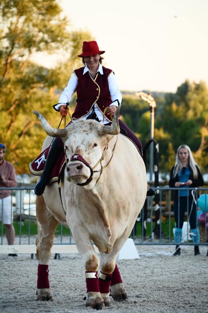 Sabine Rouas, en gilet bordeaux et chapeau rouge, montée sur Aston au soleil couchant